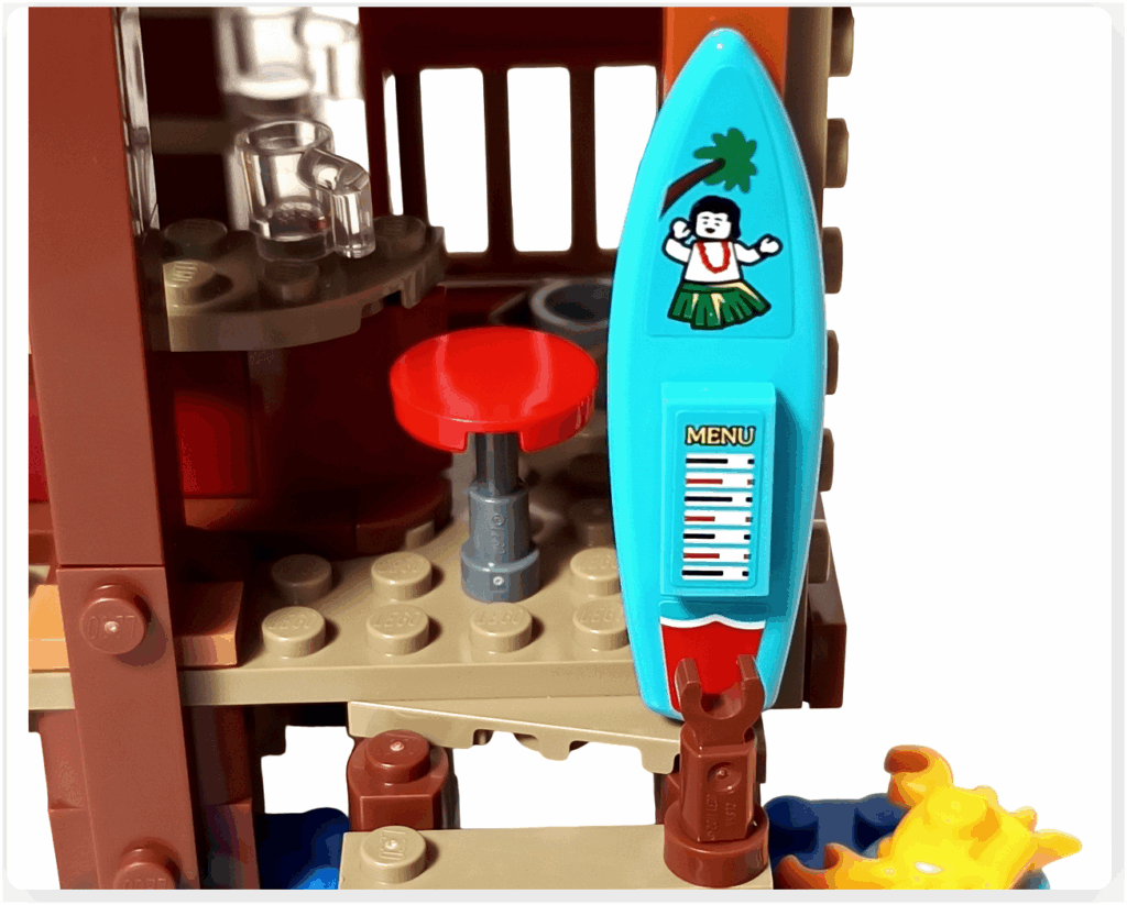 レゴ ONE PIECE 75636「フーシャ村」の入口に取り付けられたサーフボード型メニュー看板。青いサーフボードにメニュー表とフラダンス風イラストが描かれ、海辺の酒場らしい遊び心のある装飾となっている。